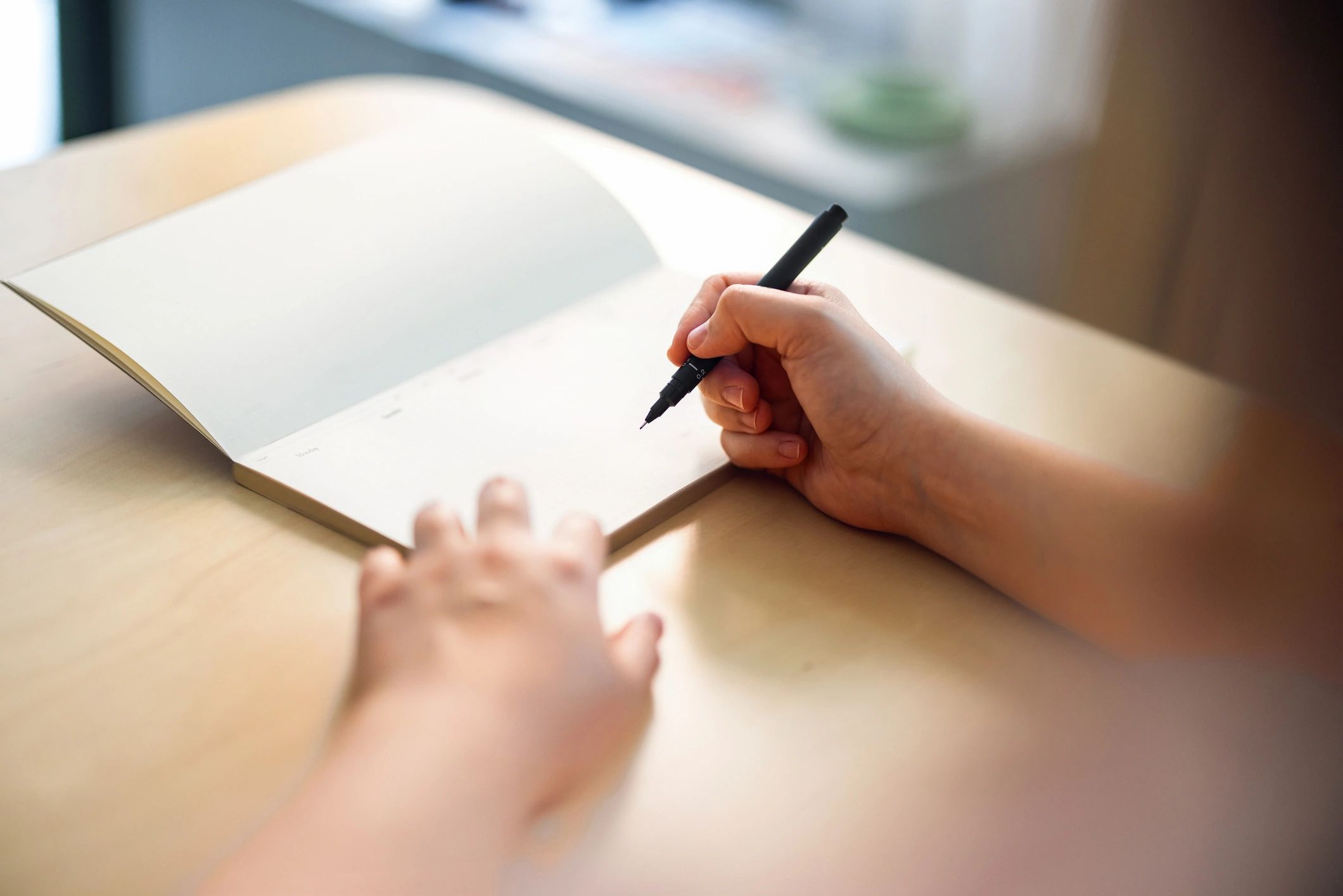 Person writing notes at a wooden desk beside books
